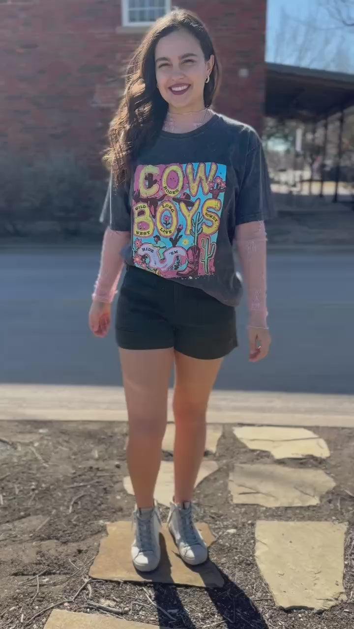 Woman wearing a graphic t-shirt and shorts standing outside.