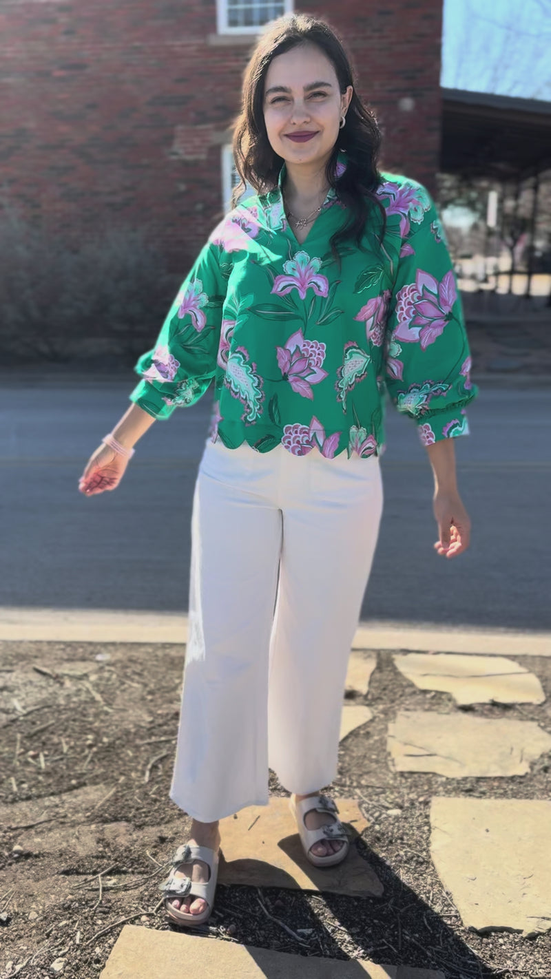 Woman wearing a green floral blouse and white pants on a sidewalk.
