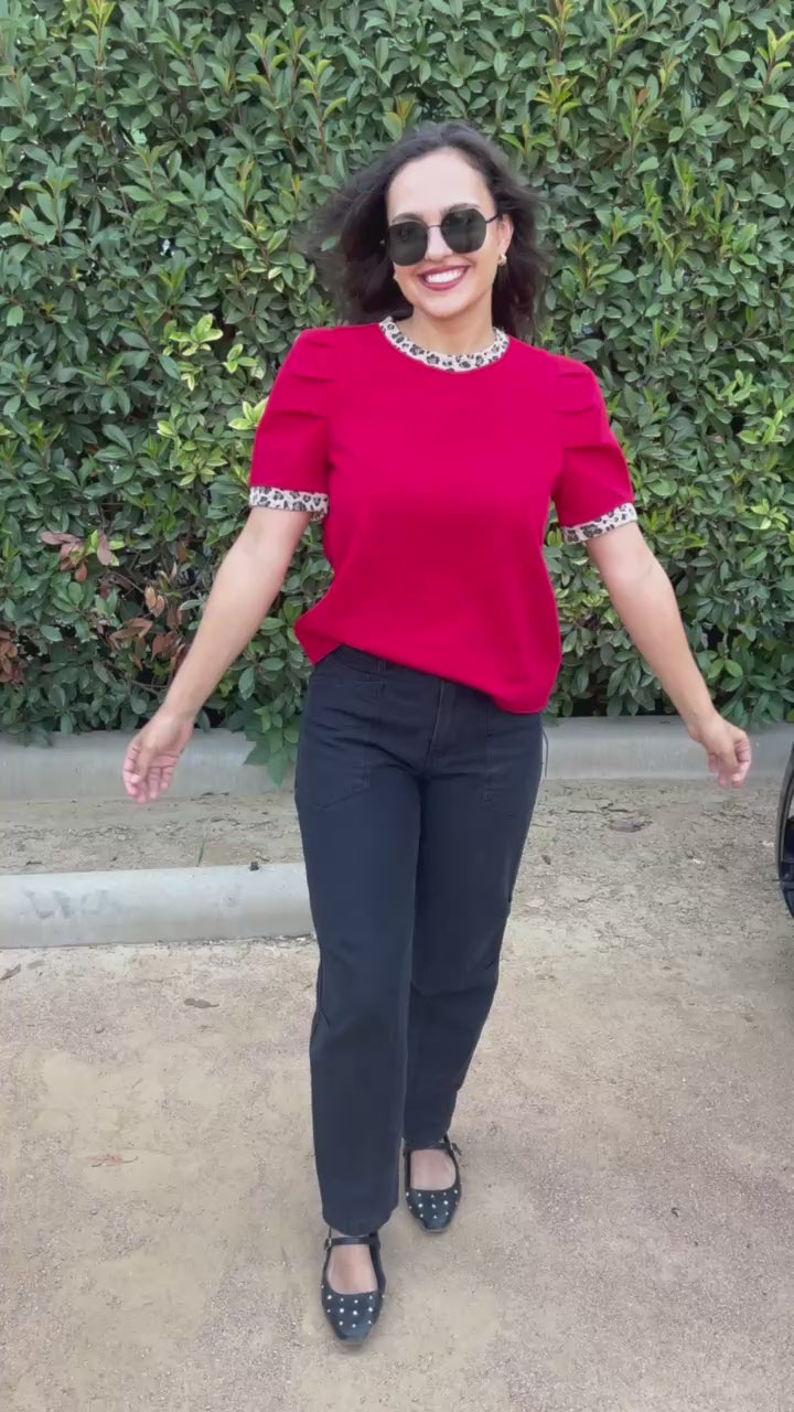 Brunette model wearing a red top with leopard trim, and black denim jeans in an outdoor setting. Southern House Clothing 
