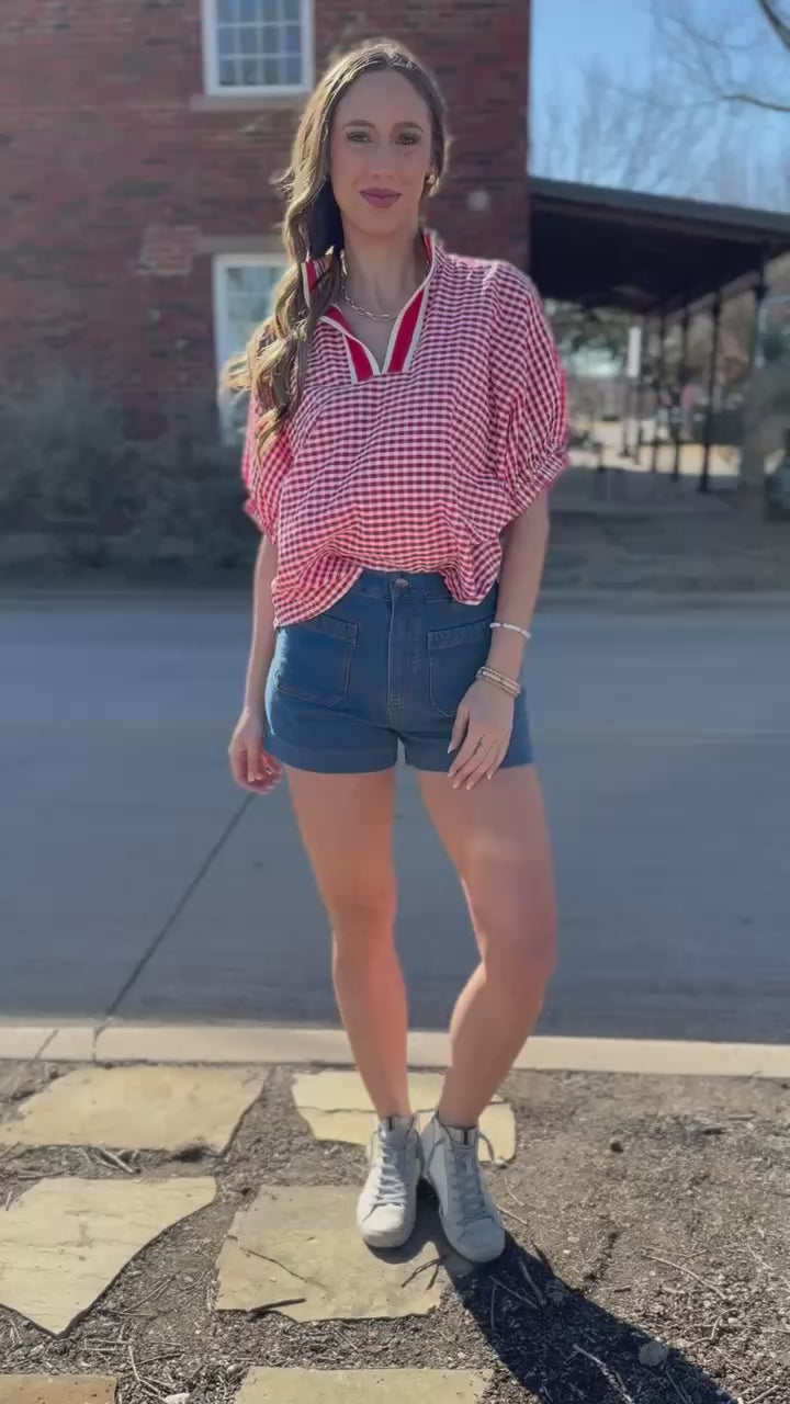 Woman wearing a red and white checkered shirt and blue shorts standing on a street.