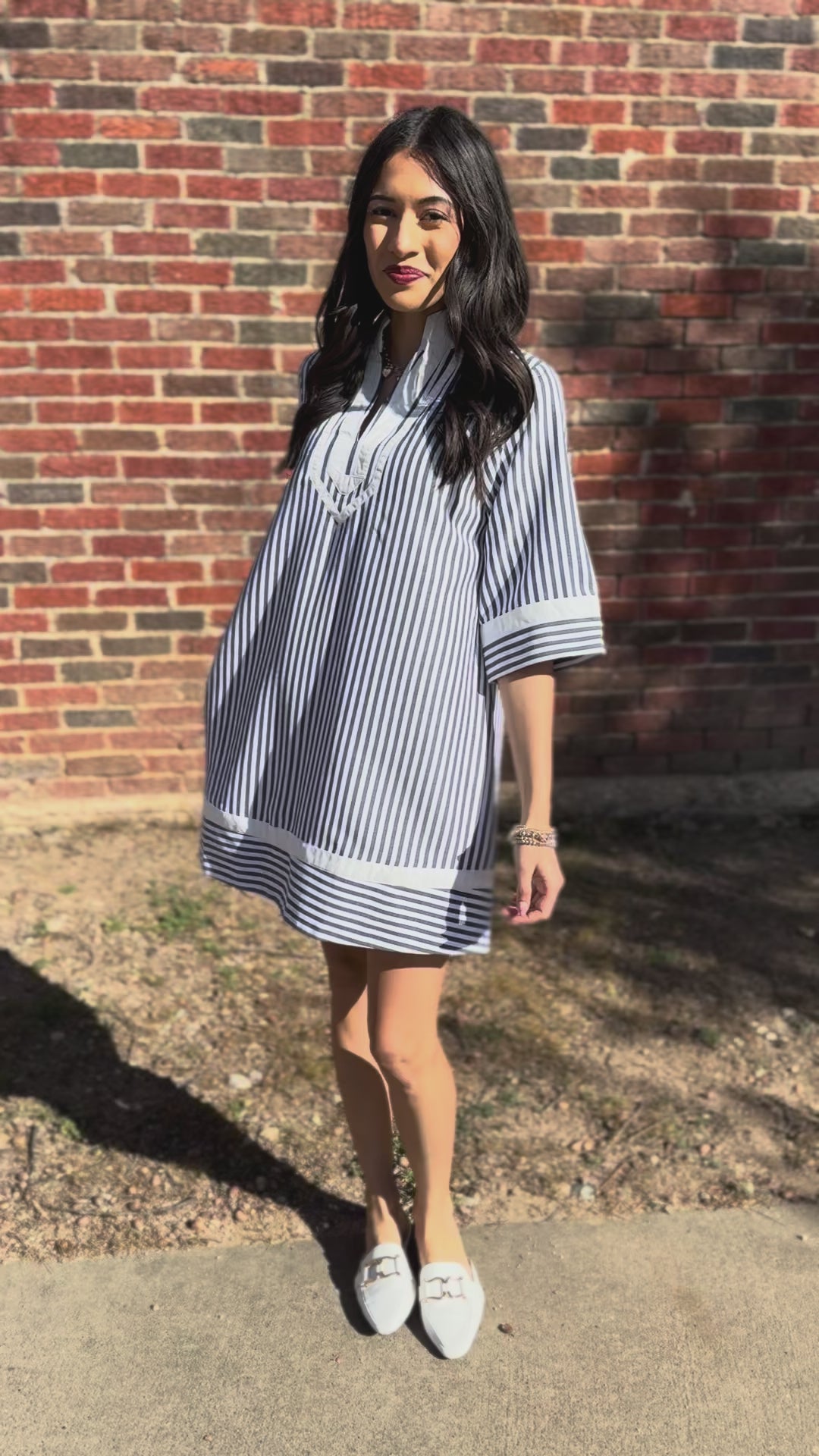 Woman wearing a black and white striped dress standing outside in front of a brick wall.