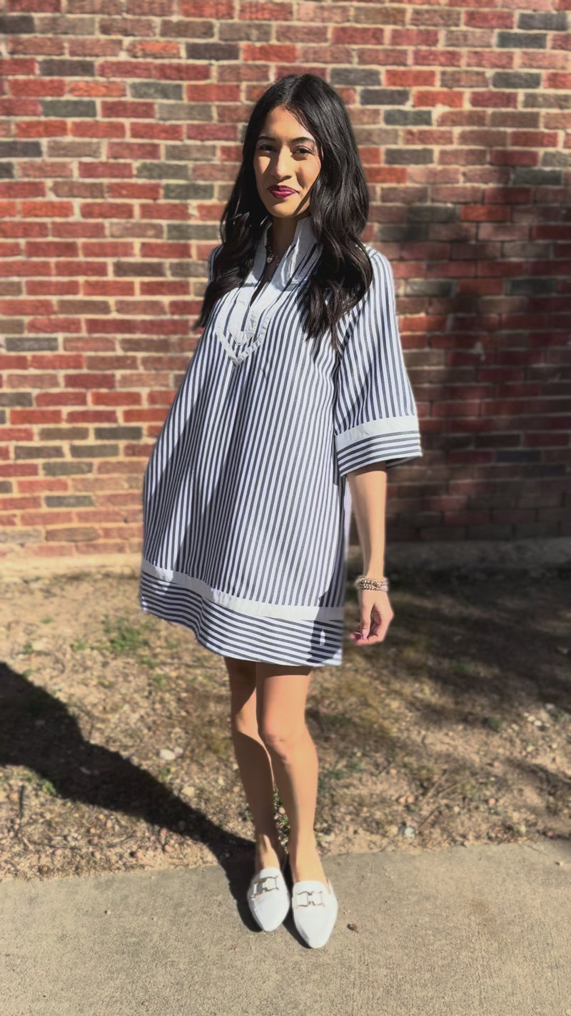 Woman wearing a black and white striped dress standing outside in front of a brick wall.