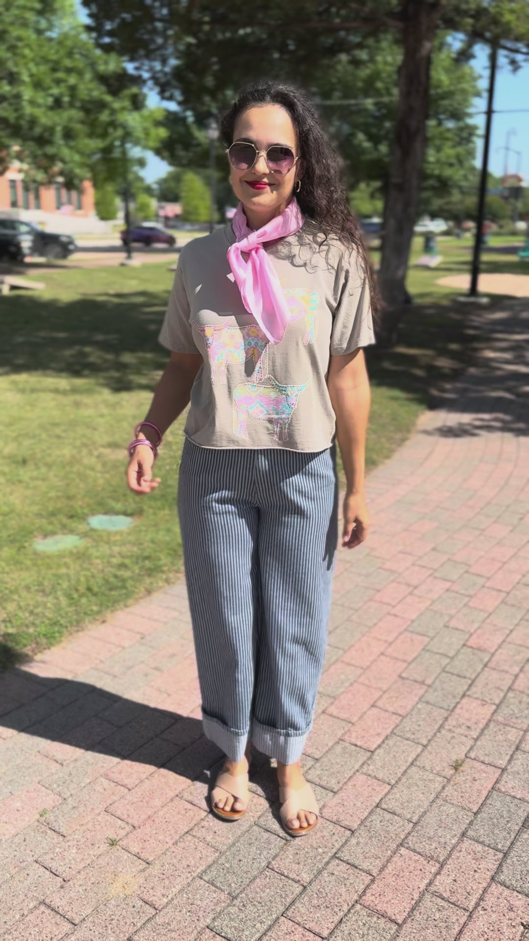 A woman wearing a beige short-sleeve top, a pink neck scarf, and blue-and-white striped pants, standing outdoors