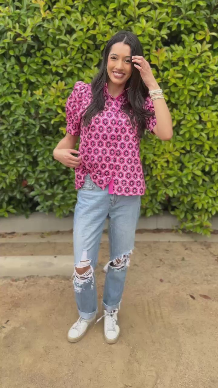 Woman wearing a pink patterned blouse and jeans standing outside.