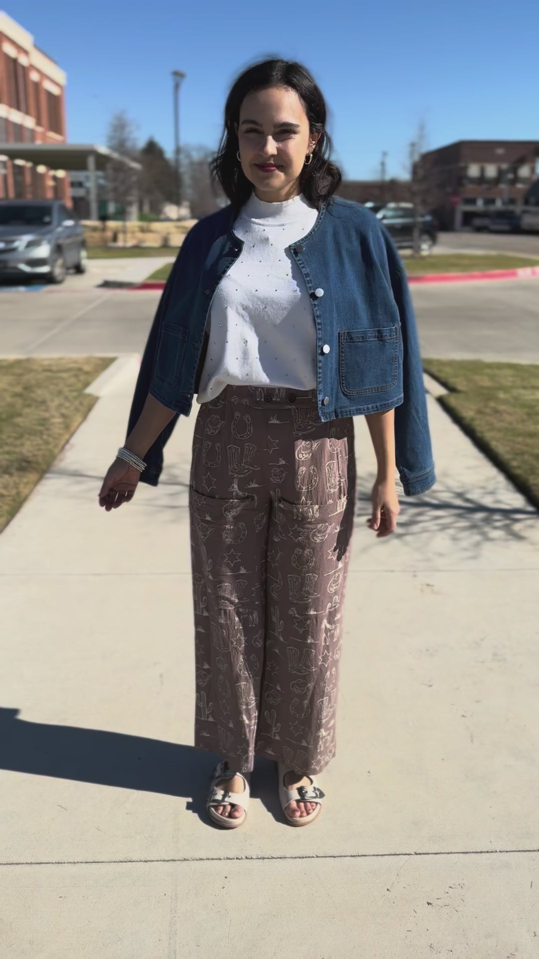 Woman wearing a white turtleneck and patterned pants standing outside.