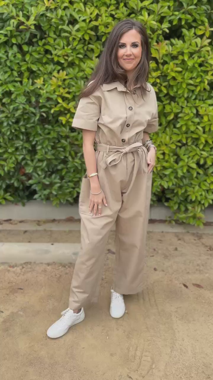 Woman wearing a beige jumpsuit standing outside.