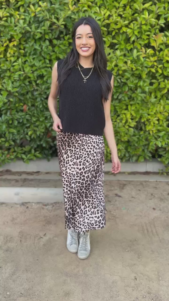 Woman wearing a black sleeveless top and leopard print skirt outdoors.