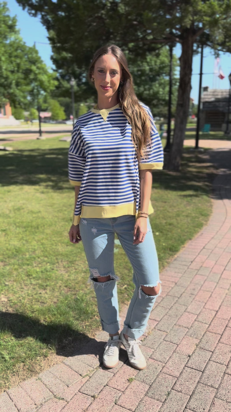 Woman wearing a blue and white striped shirt with yellow accents, standing outside.