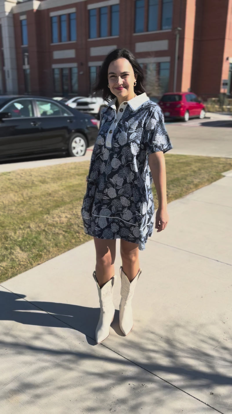 Woman wearing a blue floral dress with a white collar in an outdoor setting.