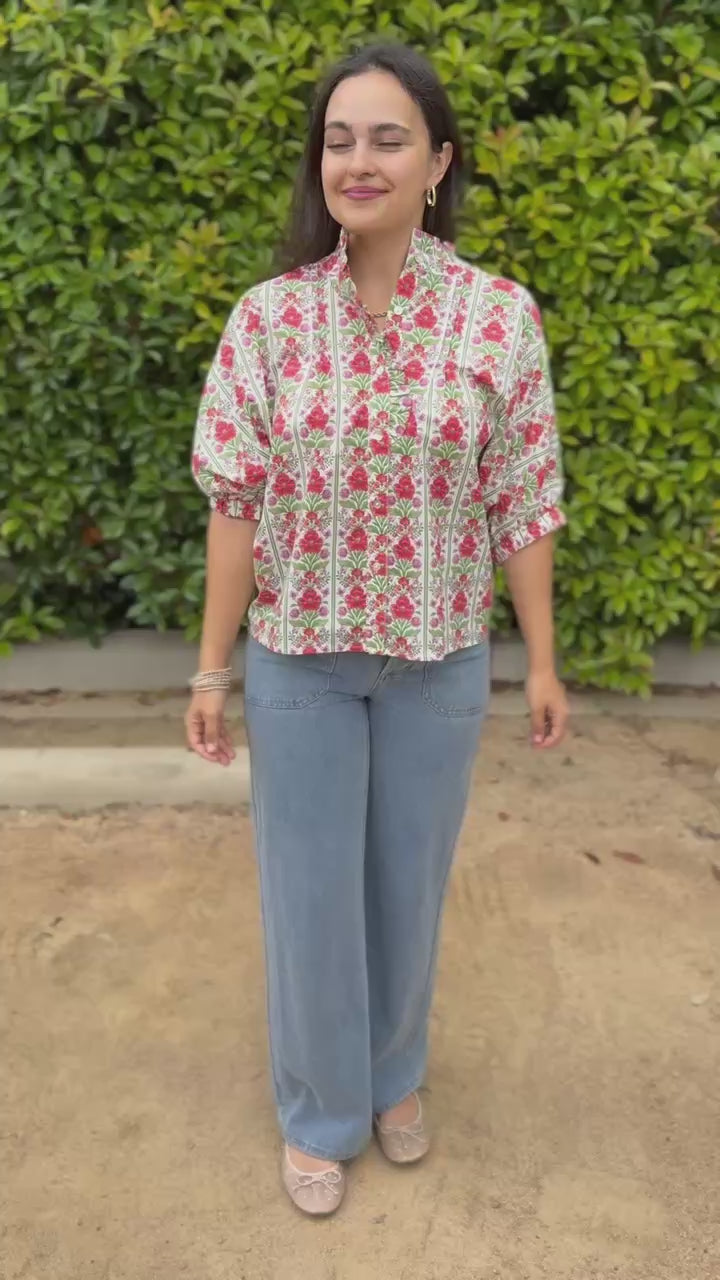 Woman wearing a floral blouse and jeans walking outdoors.