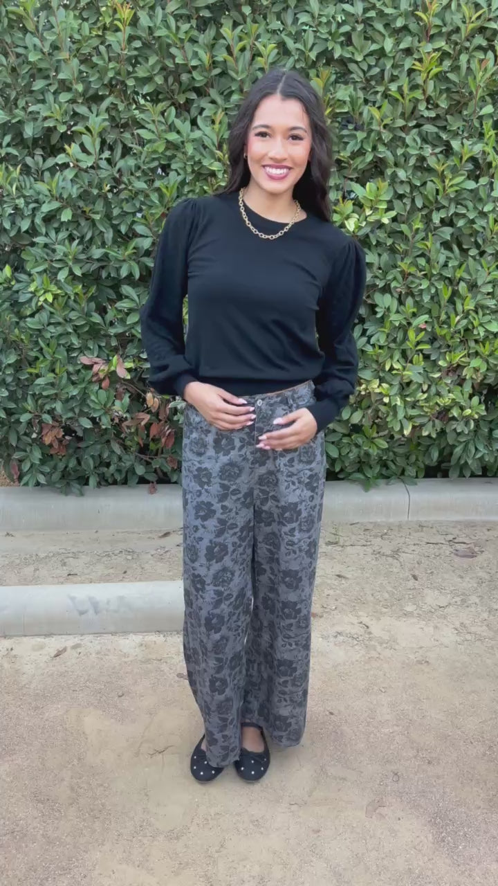 Brunette model wearing a long sleeve black top and floral print denim jeans in an outdoor setting. Southern House Clothing 