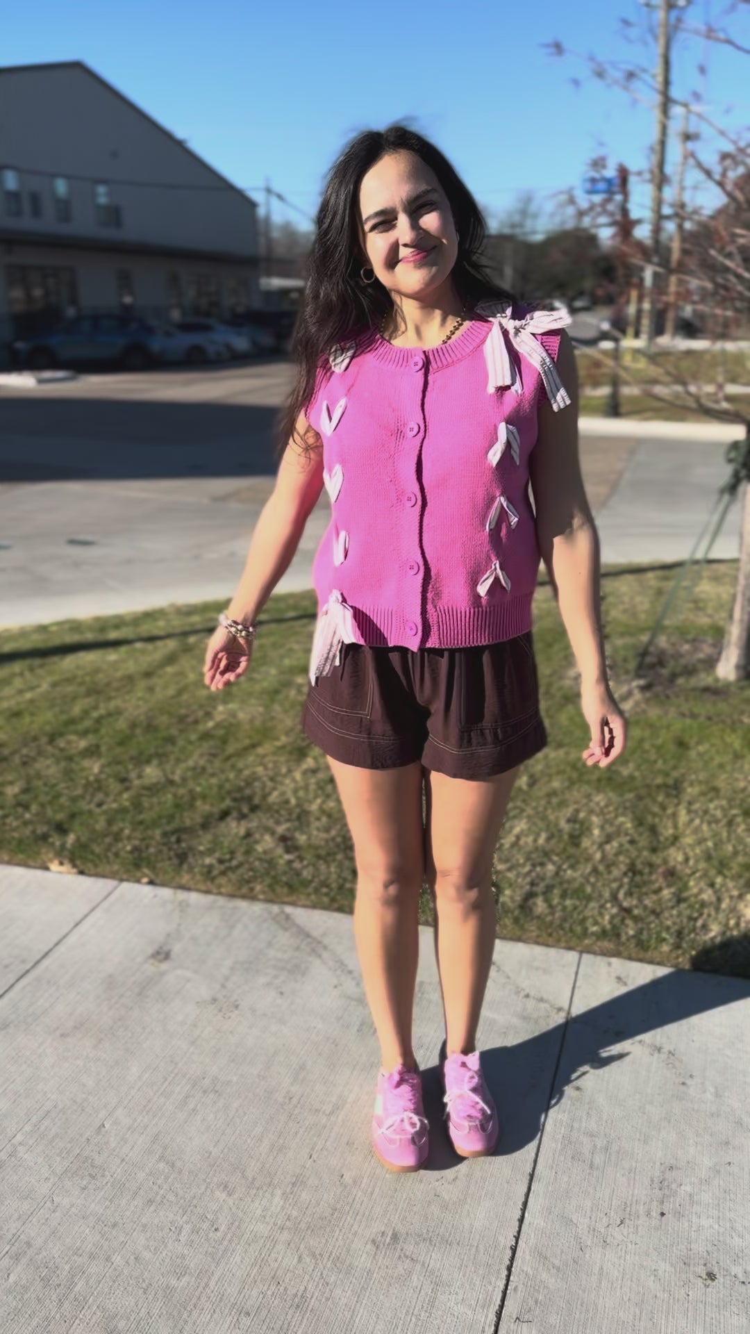 Brunette model wearing a pink sweater top and brown shorts in an outdoor setting.