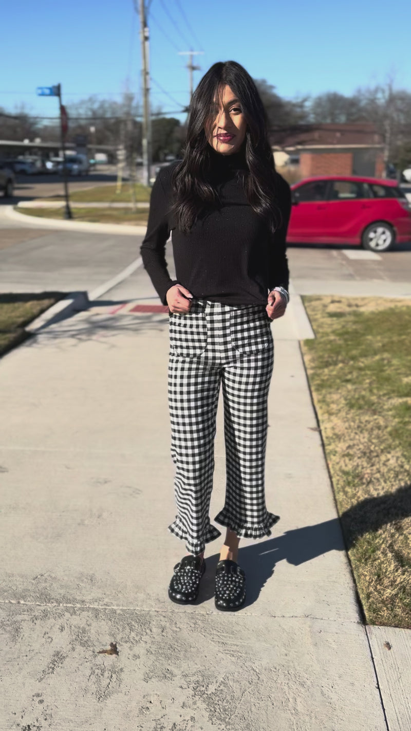 Woman wearing a black turtleneck sweater and checkered pants, standing outside.