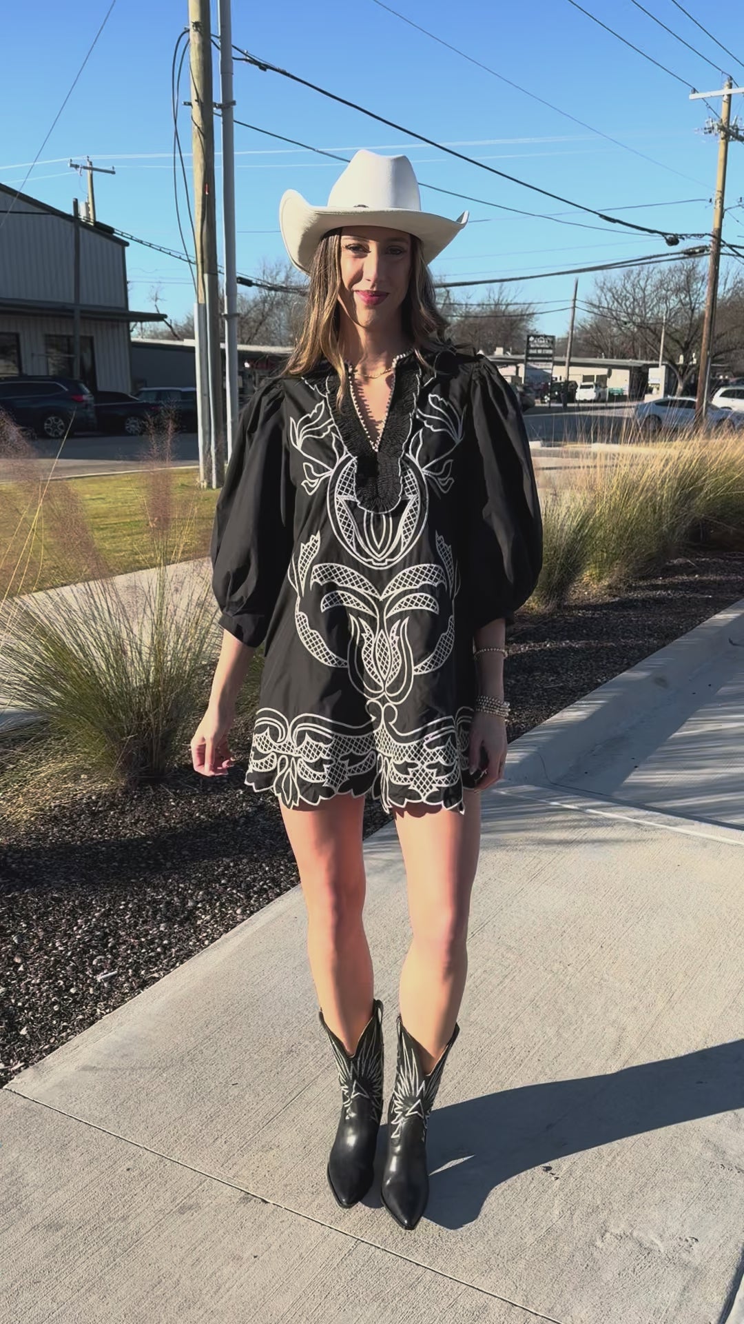 Woman wearing a black dress with white patterns and cowboy boots outside