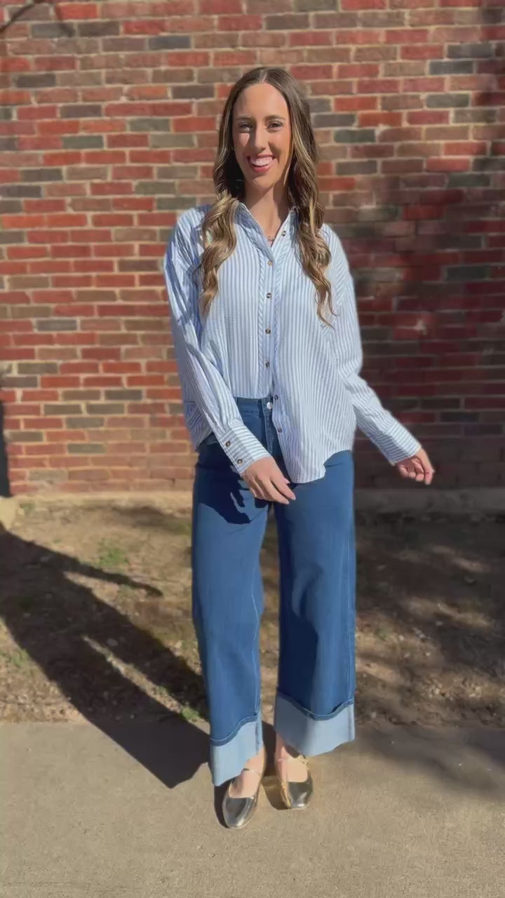 Woman wearing a white button-up shirt and blue pants standing in front of a brick wall 