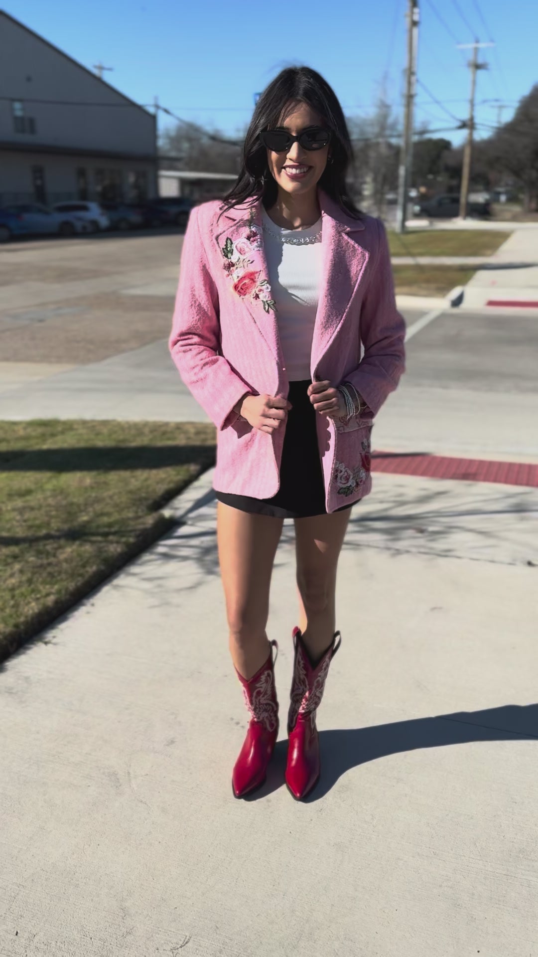 Woman wearing a pink blazer with floral embroidery outside.