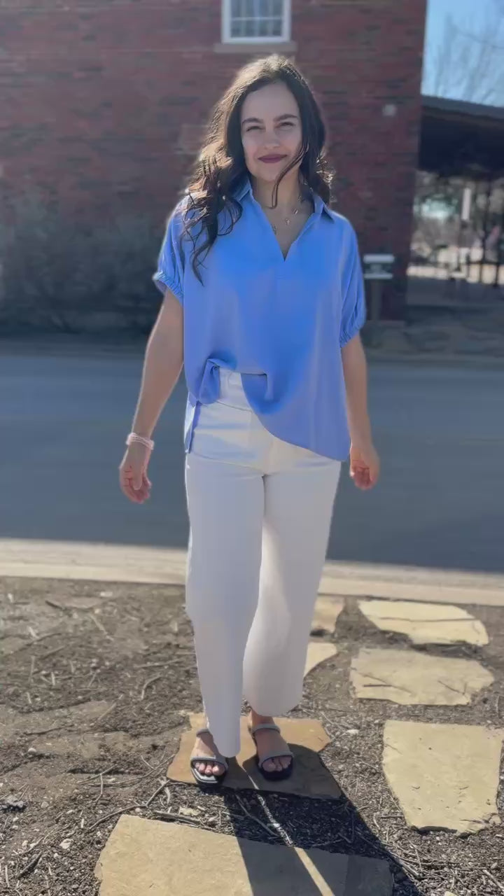 Woman wearing a light blue blouse and white pants on a city street.