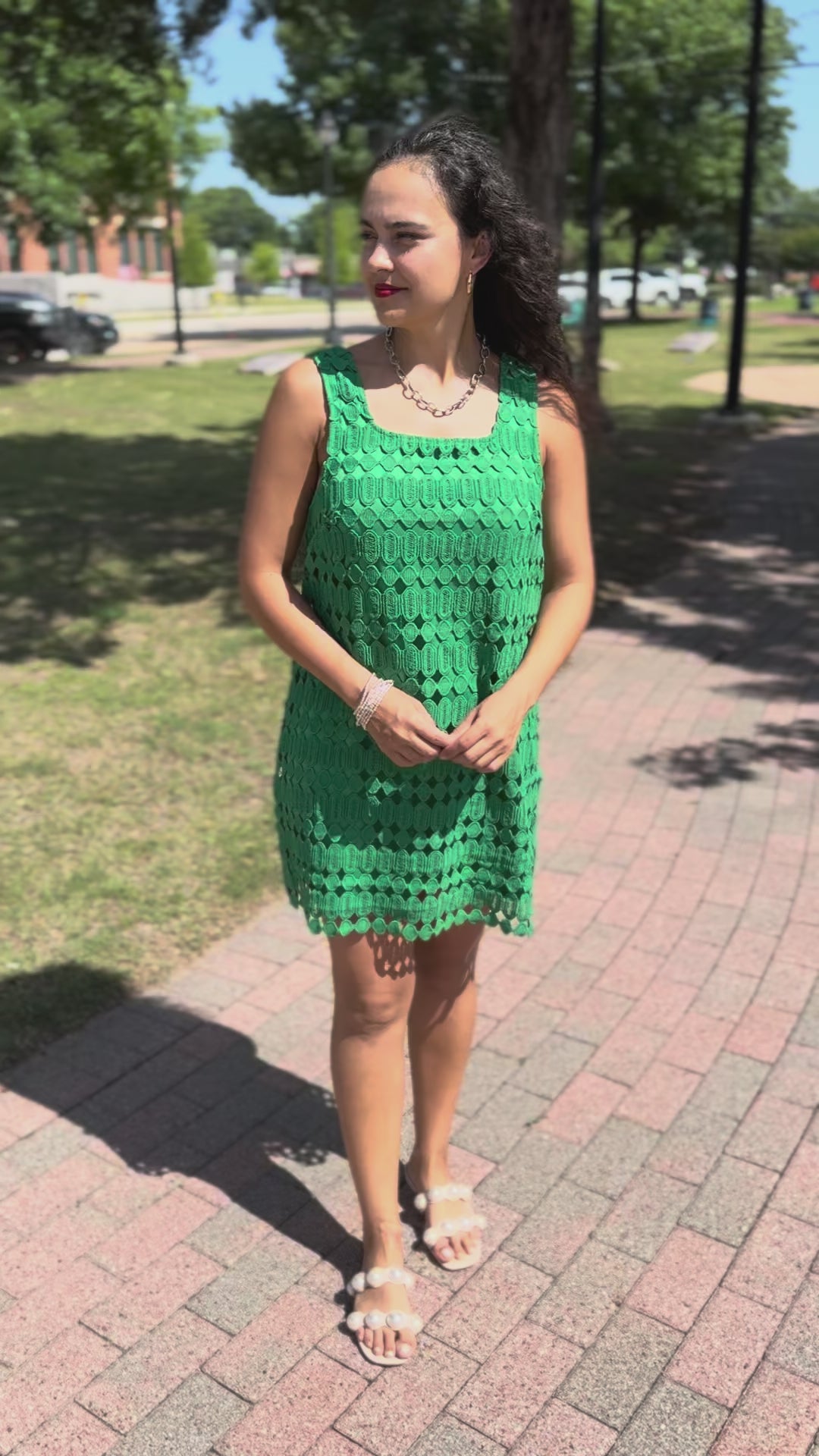 Woman wearing a green lace dress with a gold necklace standing outside.