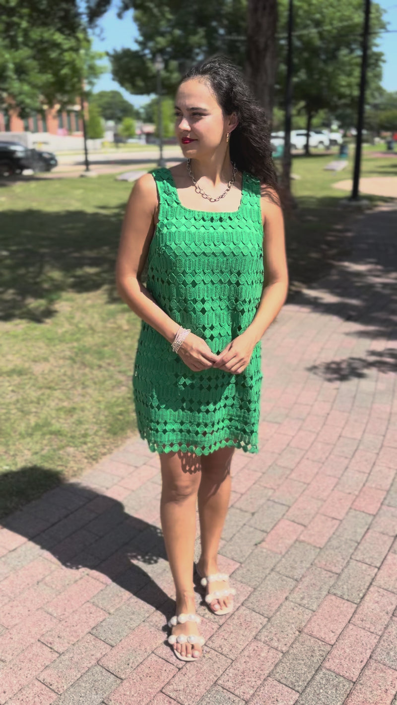 Woman wearing a green lace dress with a gold necklace standing outside.