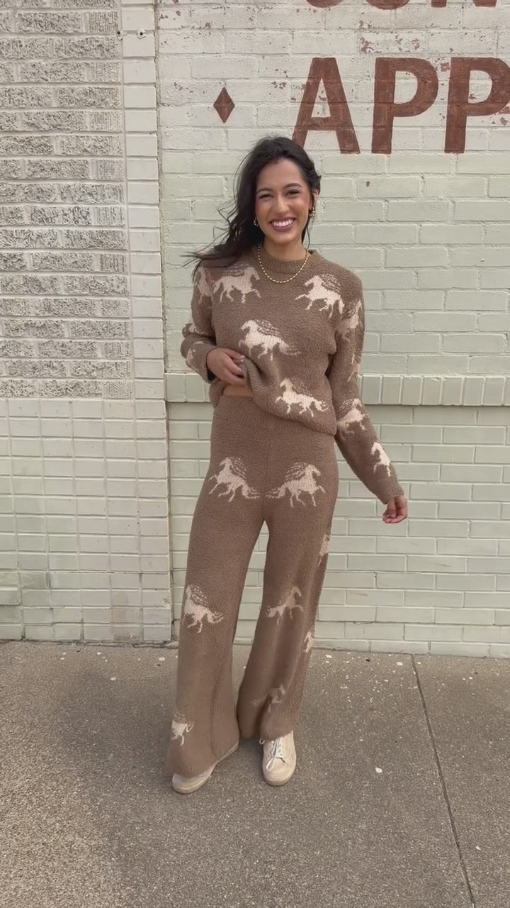 Brunette model wearing Bridlebrook Running Horse Sweater in Mocha featuring a fuzzy textured knit, cream running horse pattern, crew neckline, and long sleeves. it is paired with the Bridlebrook Running Horse Pants with the same pattern to make a set. Southern House Clothing