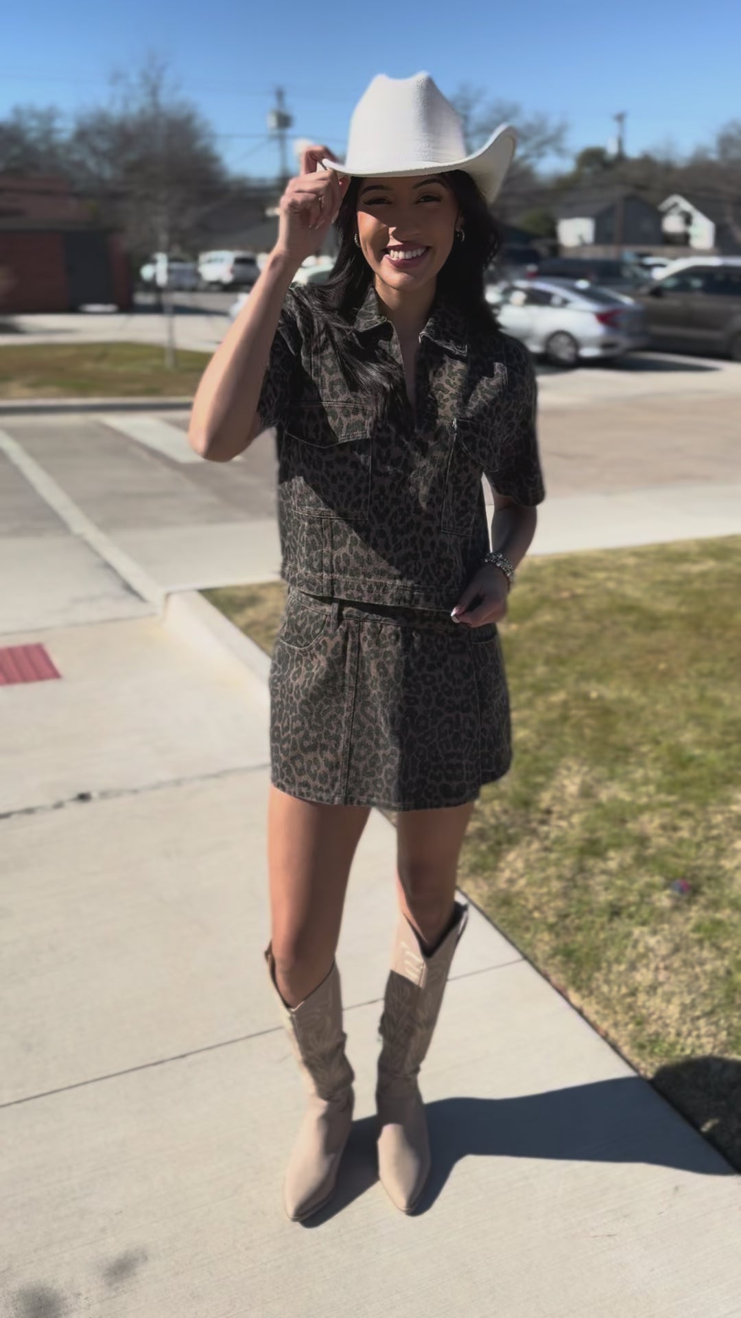 Woman wearing a leopard print outfit with a cowboy hat outside.