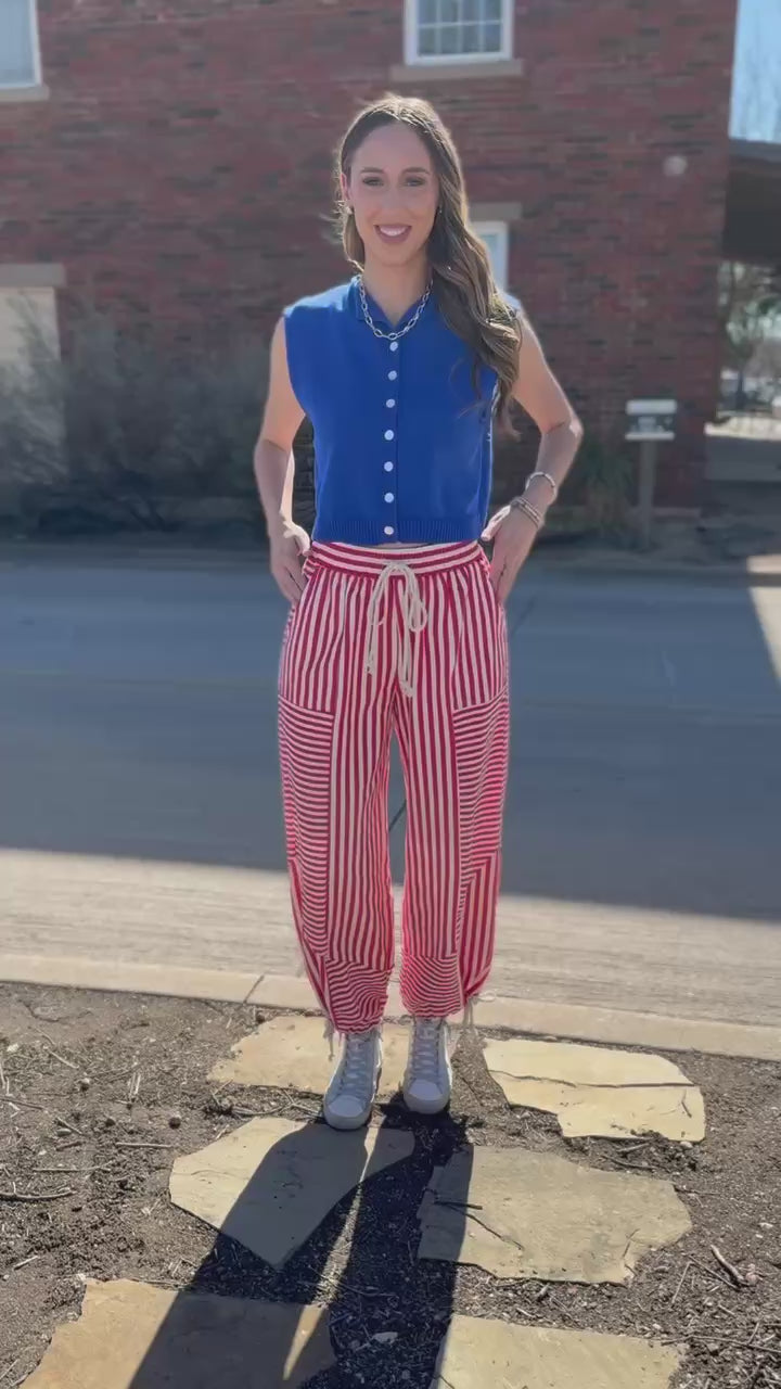 Woman wearing a blue sleeveless cardigan and red and white striped pants on a street.