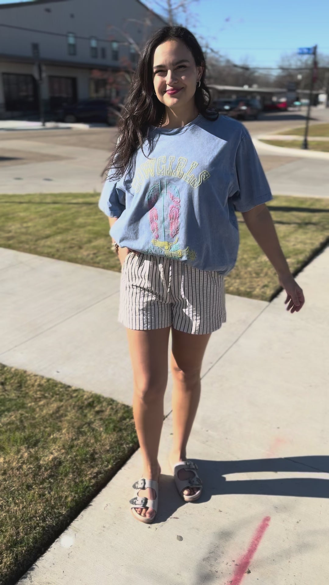 Person wearing a blue graphic t-shirt with a cowboy boot design outside.