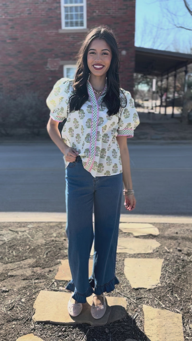 Woman wearing a patterned blouse and blue jeans on a city street.