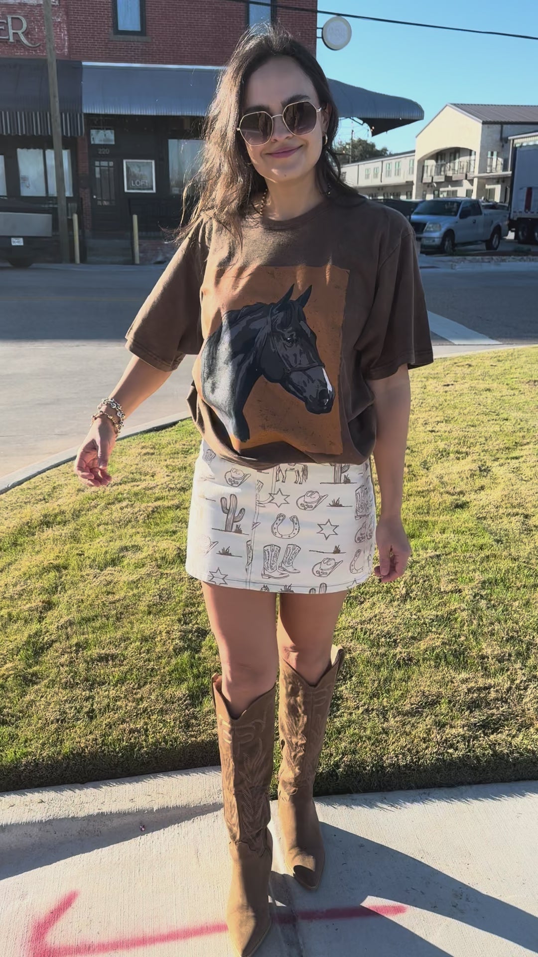 Woman wearing a graphic t-shirt with a horse design, white lace skirt, and brown boots outside