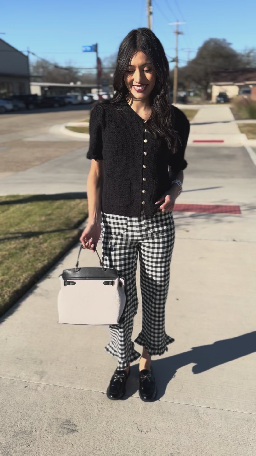 Woman wearing a black cardigan with white buttons and gingham pants, standing outdoors.