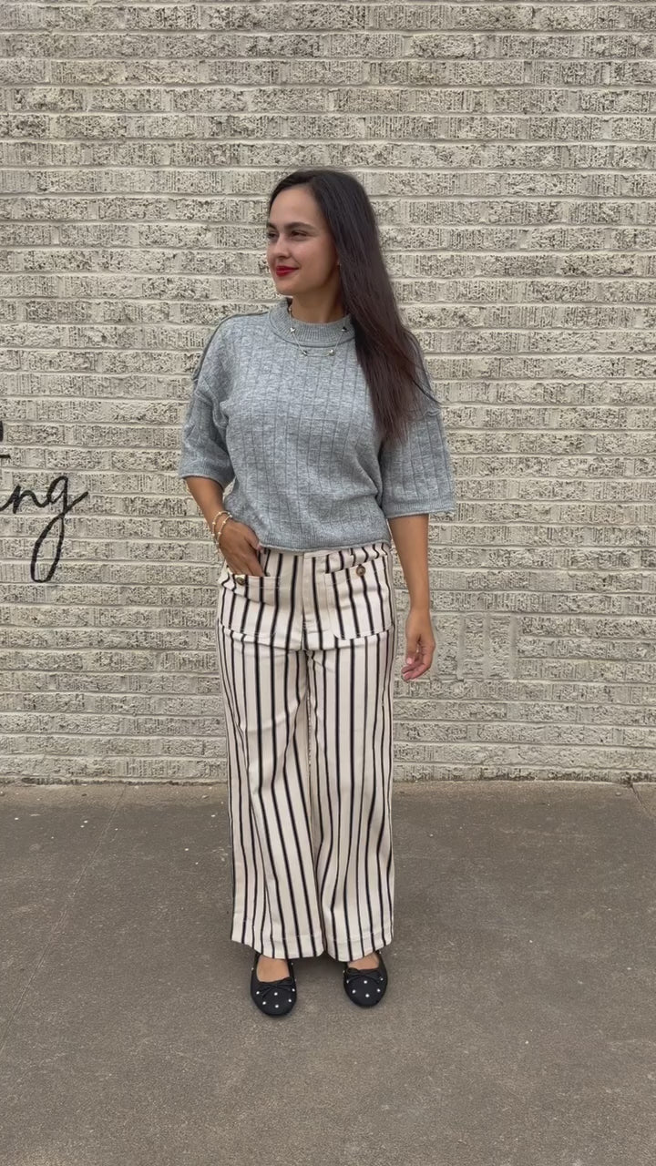 Brunette model wearing the Whitlock Grid Knit Top in Heather Gray featuring a textured grid pattern, round neckline, dropped shoulders, and elbow-length sleeves, styled with cream and black striped wide-leg pants called the Bristols. Southern House Clothing.