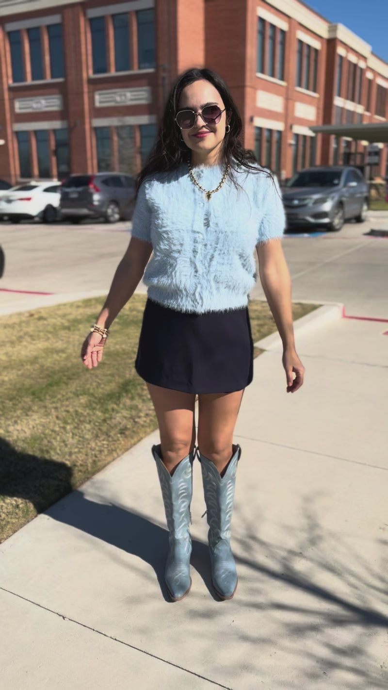 Woman wearing a light blue top and navy skirt outdoors.