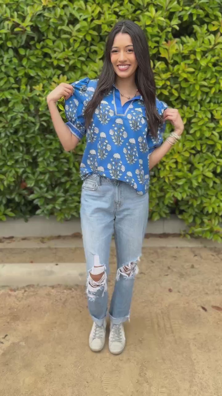 Woman wearing a blue floral blouse and light blue jeans standing outdoors.