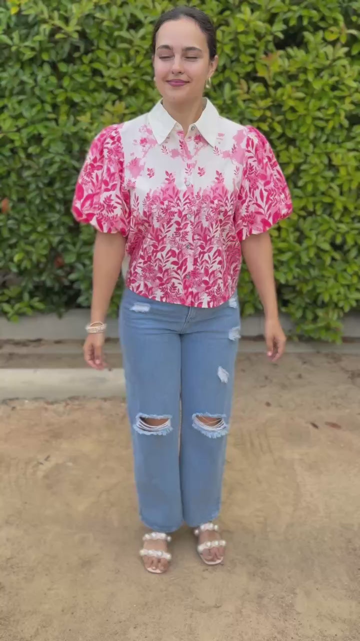 Woman wearing a pink floral blouse and blue jeans outdoors.