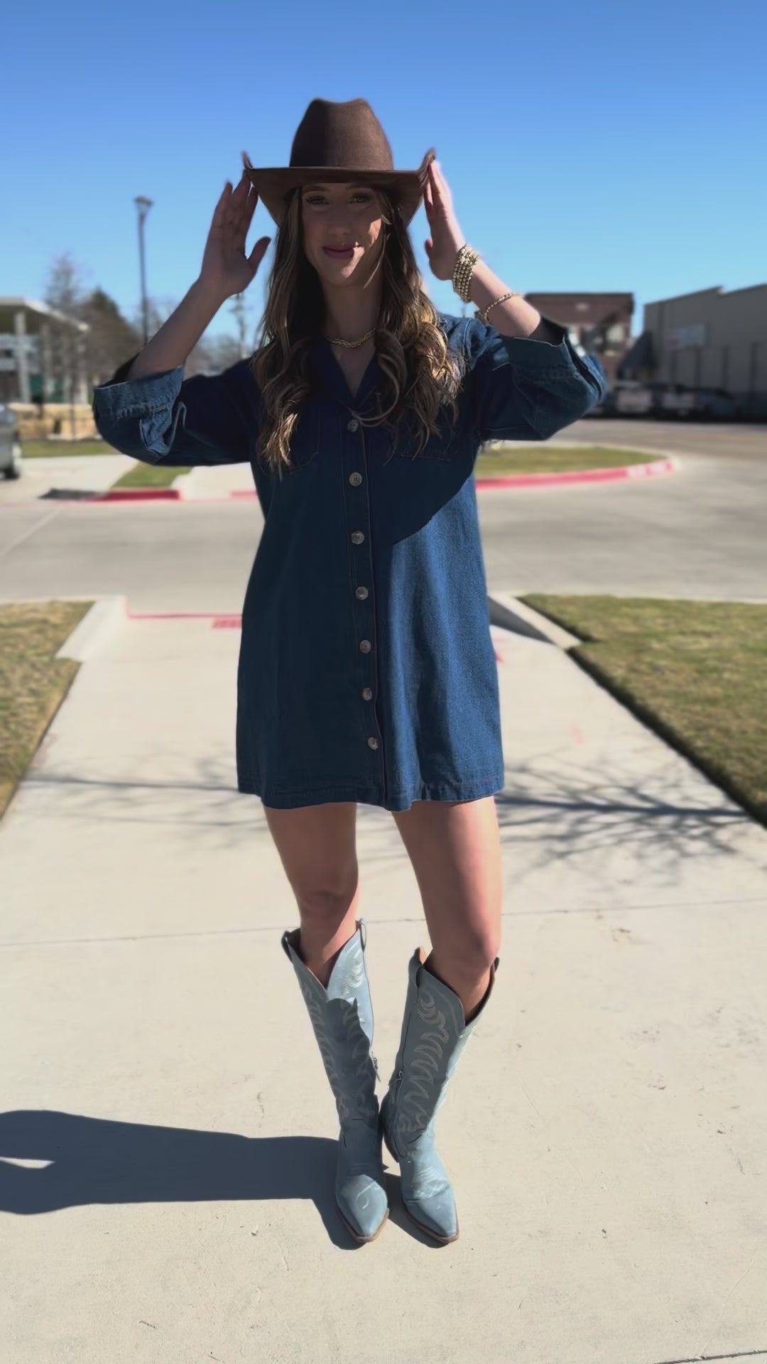 Woman in a blue dress and cowboy hat standing outside.
