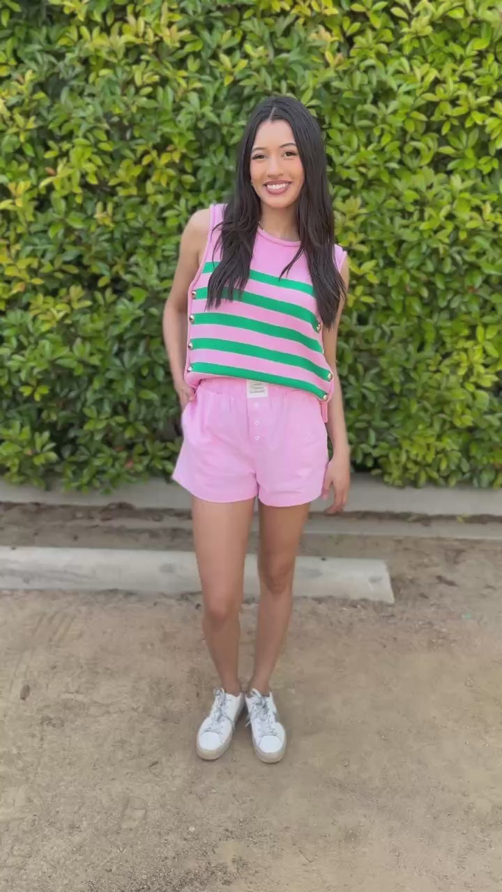 Woman wearing a pink and green striped top with pink shorts outdoors.