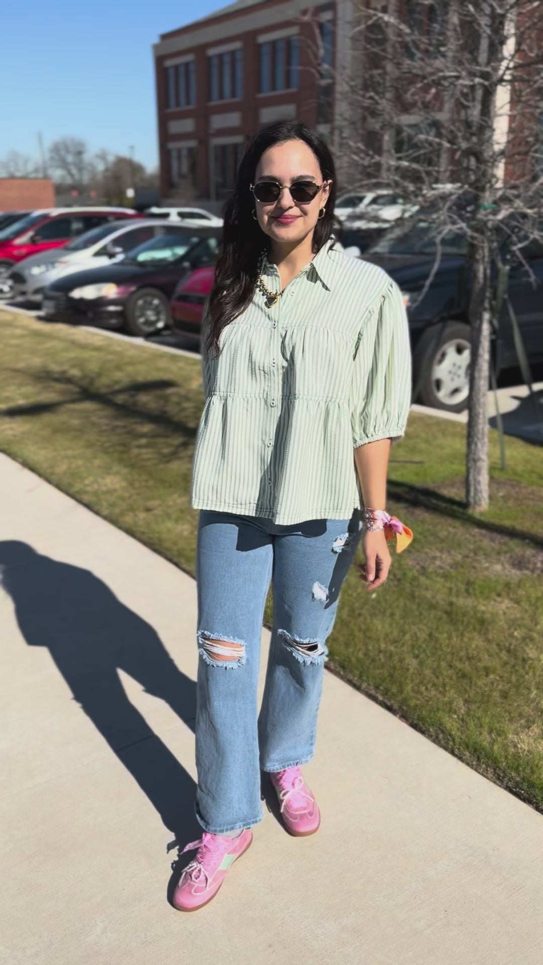 Woman in light-colored shirt and ripped jeans standing on a sidewalk.