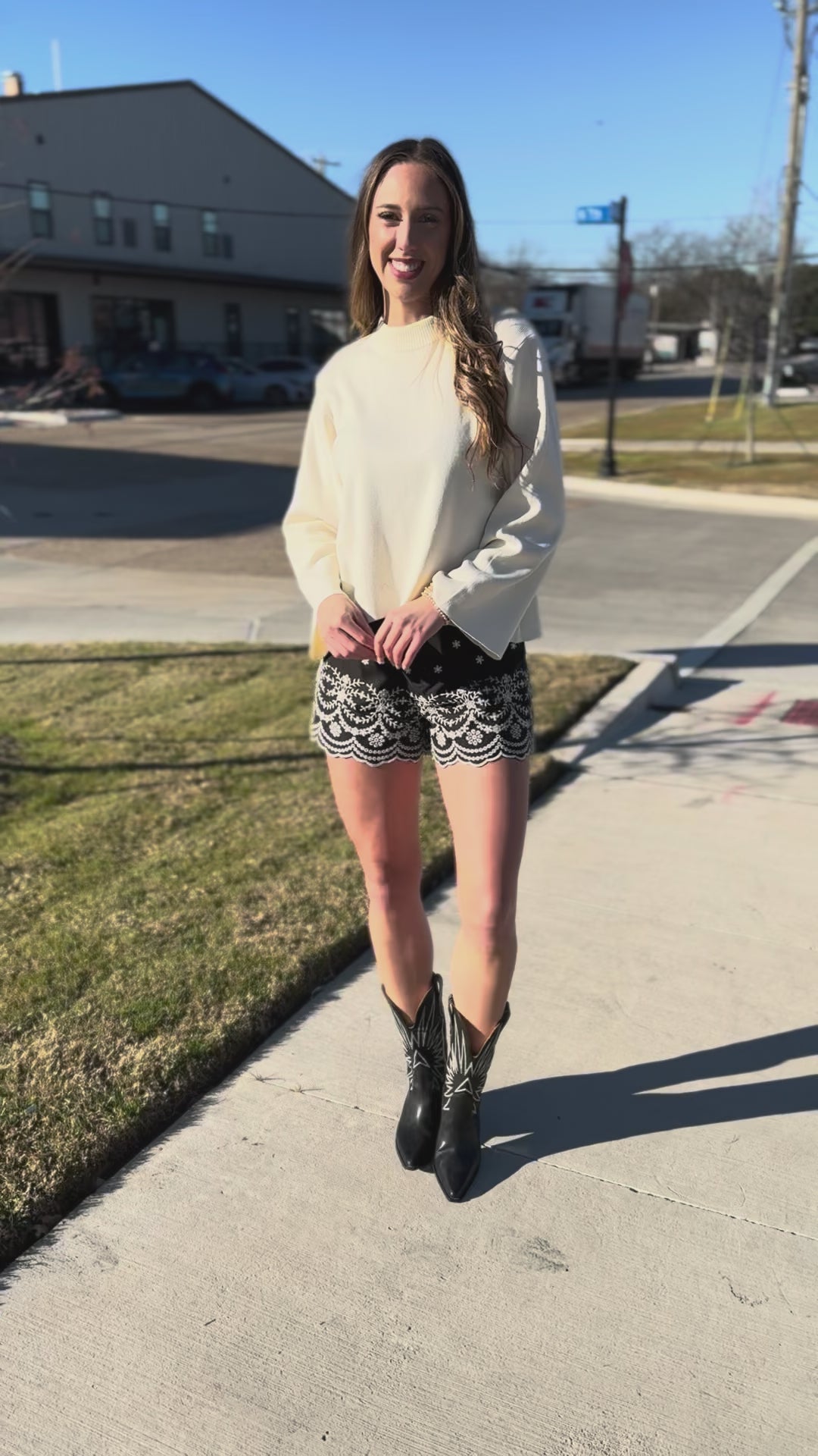 Woman wearing a white sweater and black shorts with white lace trim outdoors.