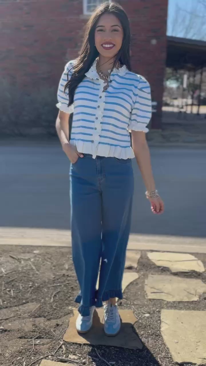 Woman wearing a striped shirt and blue jeans on a city street.