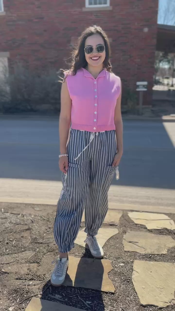 Woman wearing a pink sweater tank and blue and whit striped pants outside.