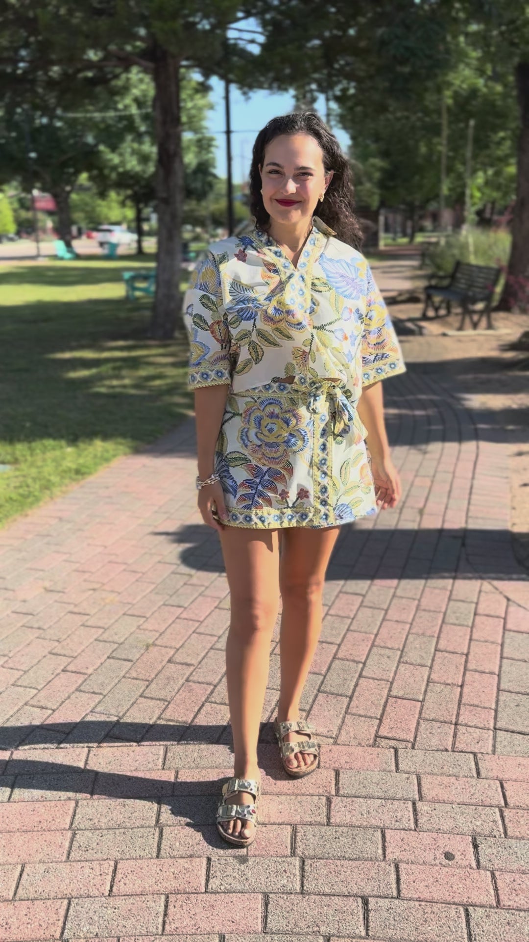 Woman in a floral set standing outside on a sidewalk.