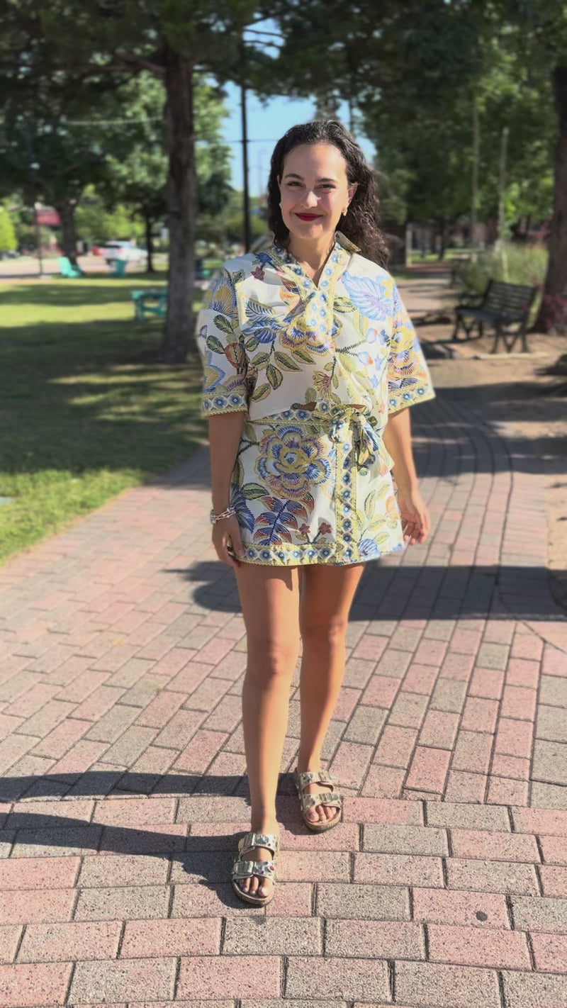 Woman in a floral set standing outside on a sidewalk.