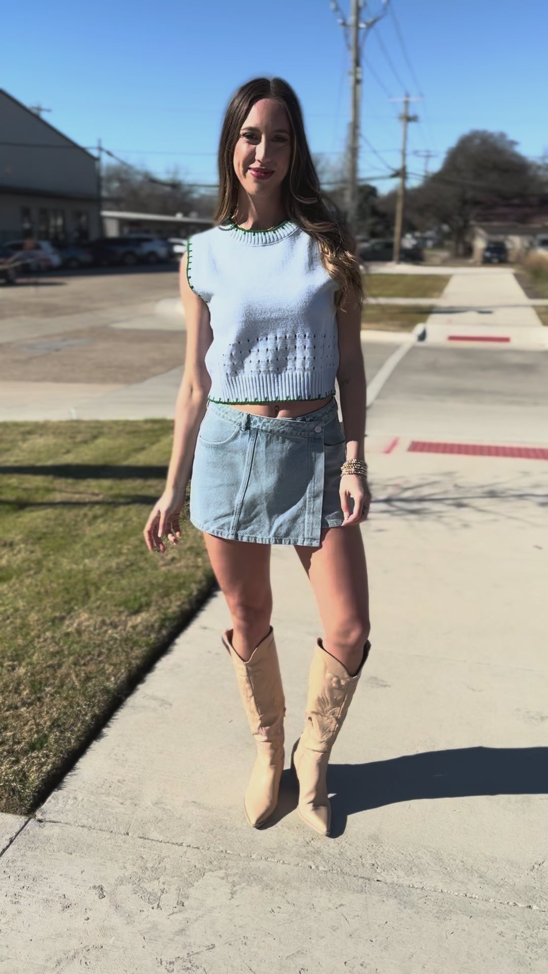 Woman wearing a light blue sleeveless top and denim skirt outdoors.