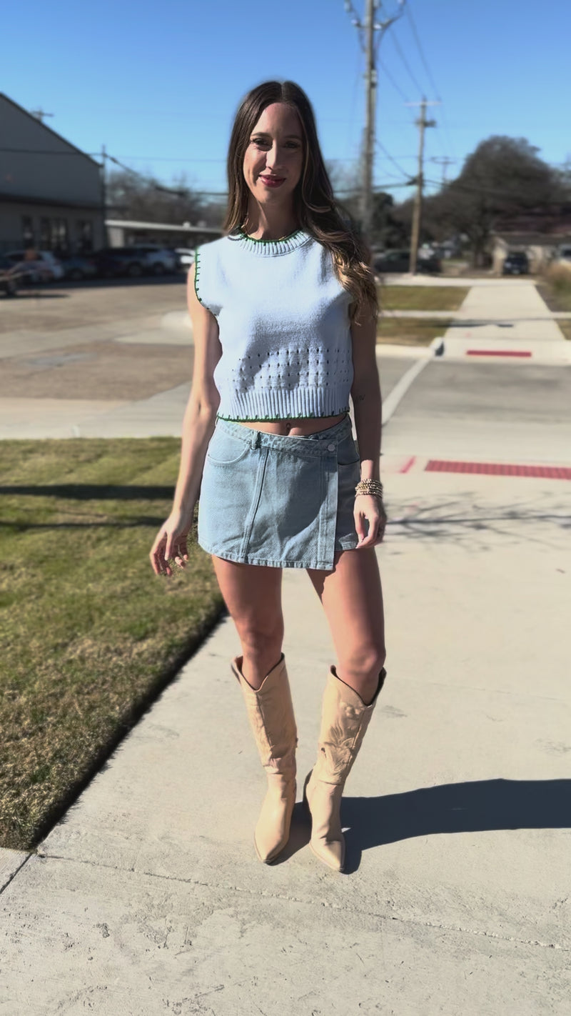 Woman wearing a light blue sleeveless top and denim skirt outdoors.