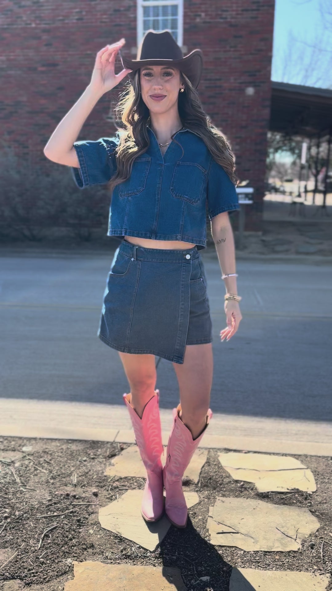 Woman wearing a denim outfit with a cowboy hat and pink shoes on a street.