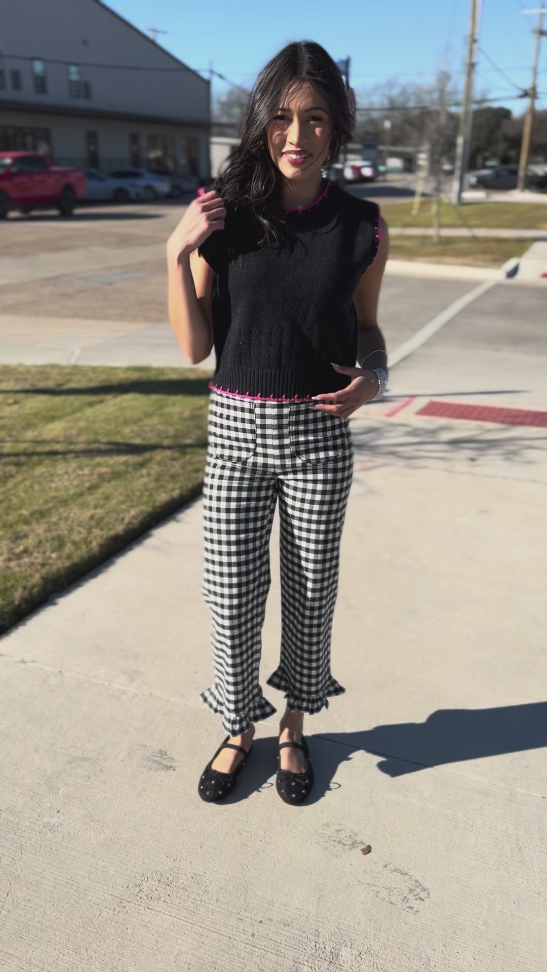 Woman wearing a black sleeveless top with pink trim and checkered pants outside.