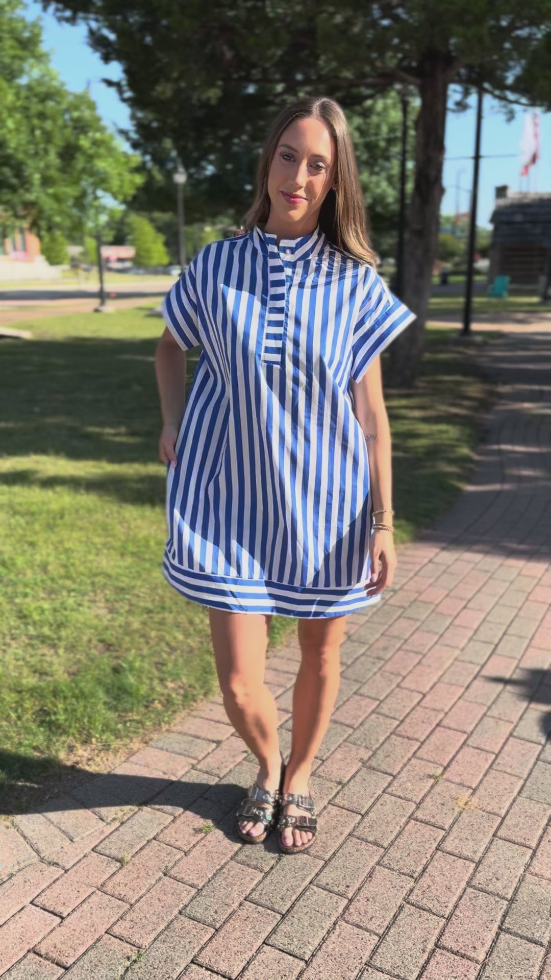 Woman wearing a blue and white striped dress with sunglasses and sandals, standing on a street