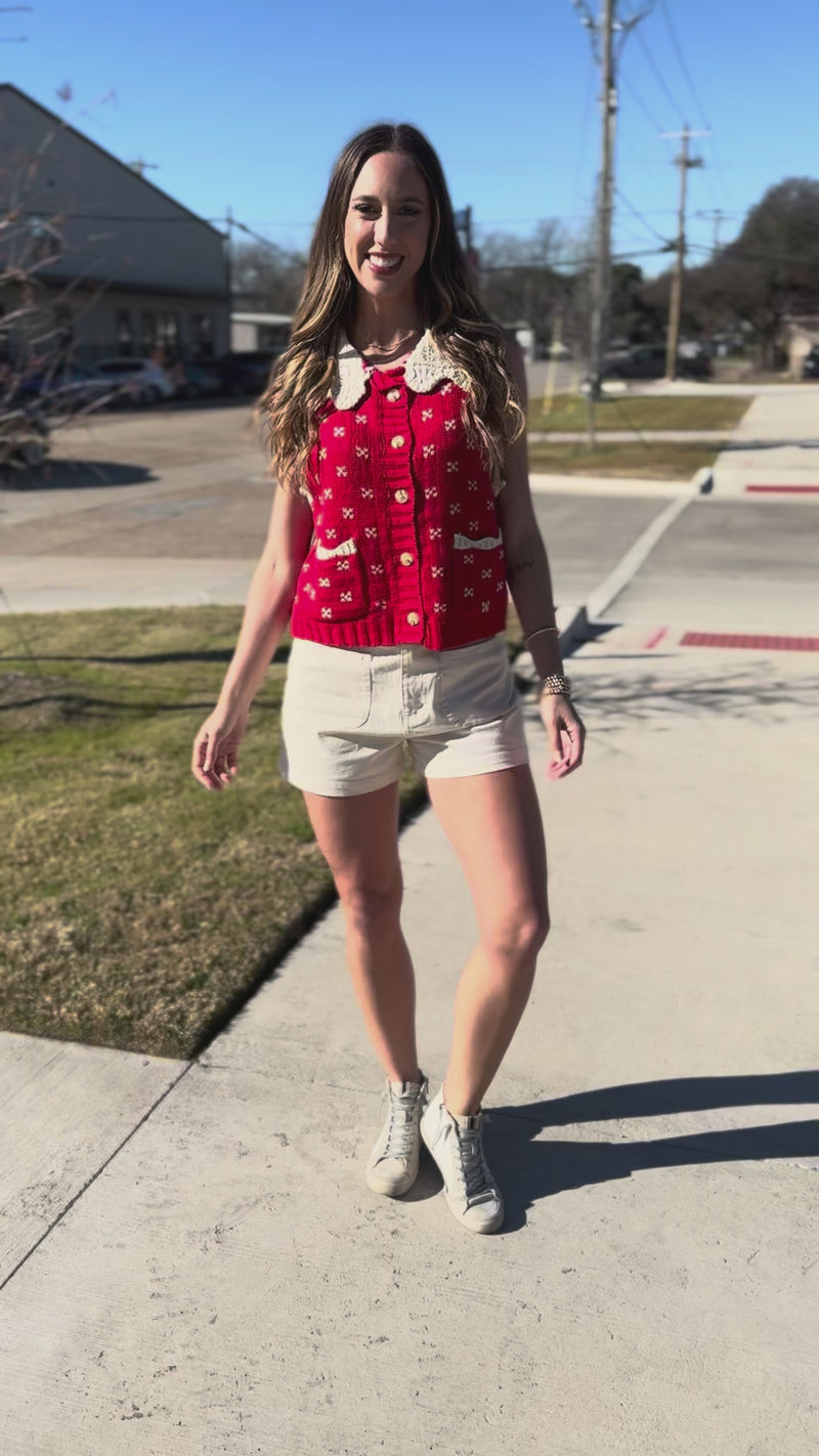 Woman wearing a red patterned top and white shorts outdoors.