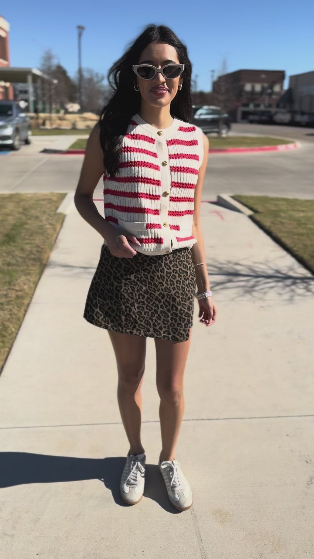 Woman wearing a red and white striped sleeveless shirt, leopard print skirt, and white sneakers outside.