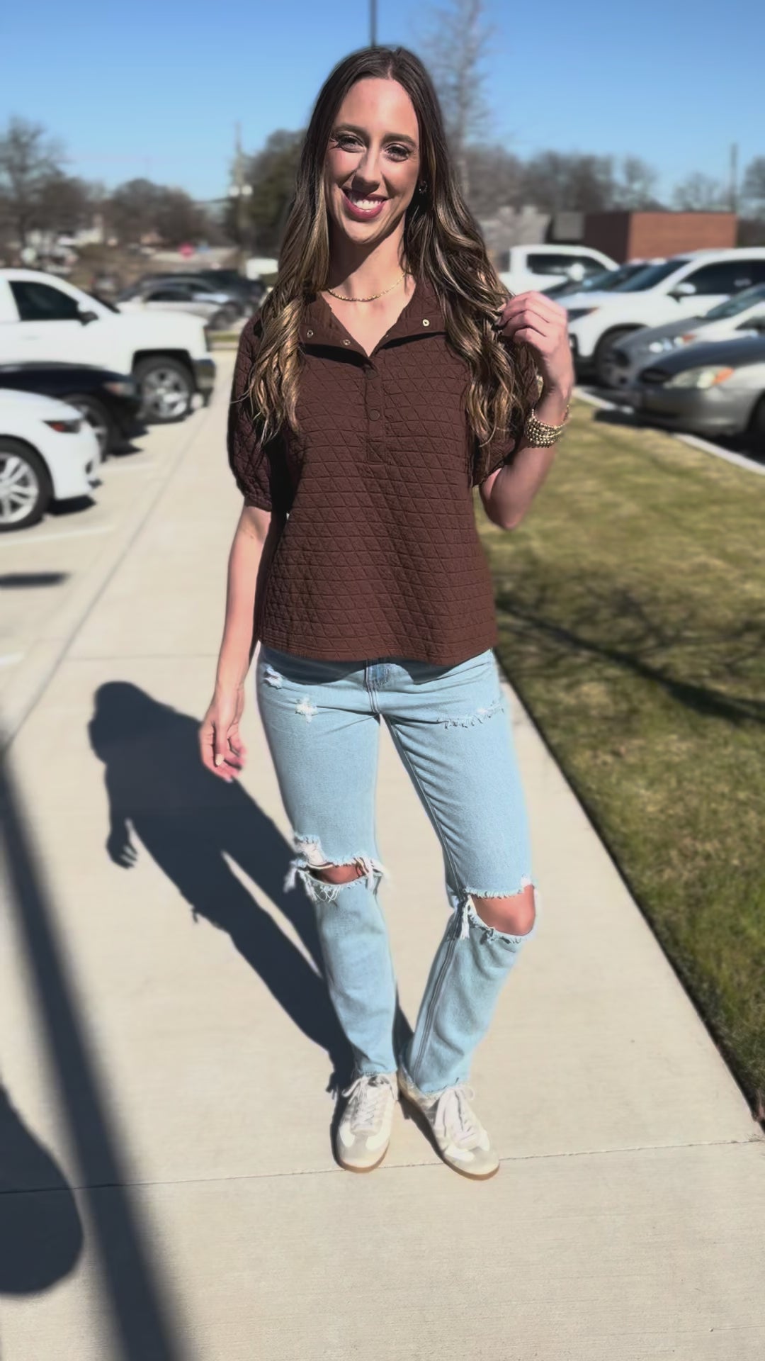 Woman wearing a brown textured shirt and light blue jeans outdoors.